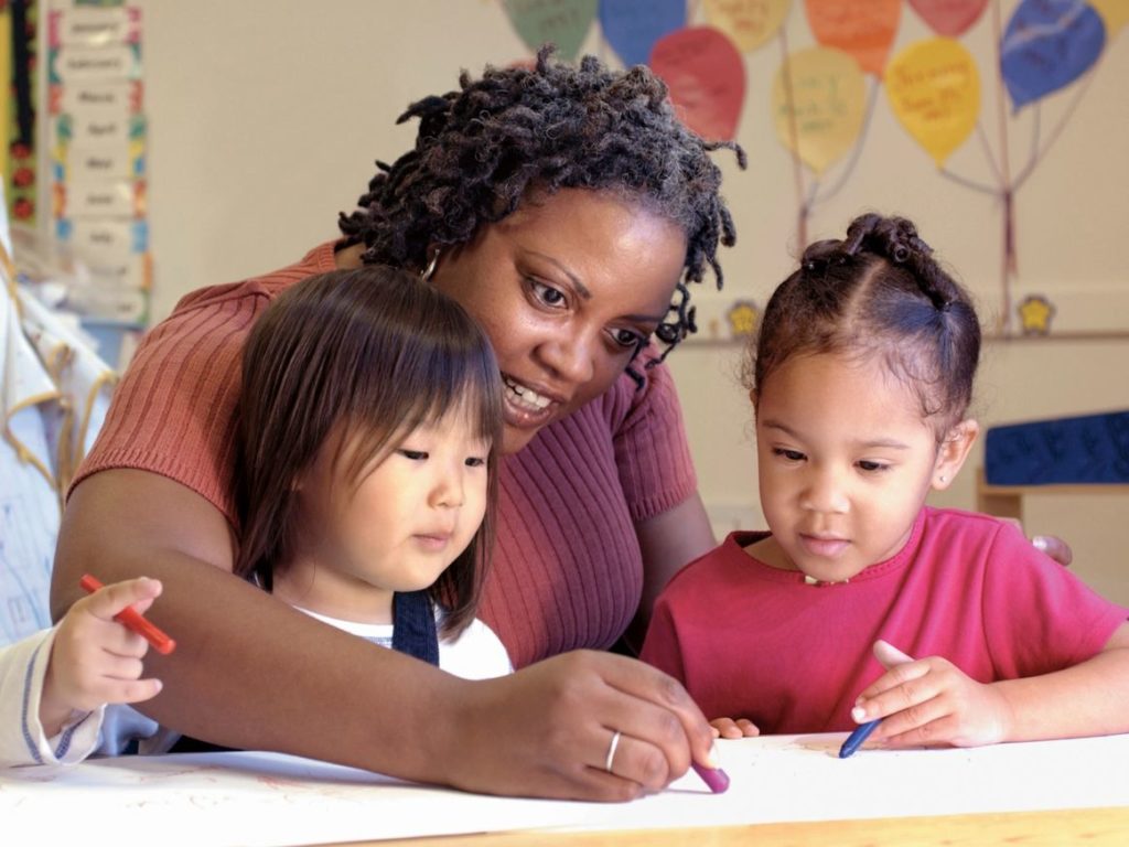 A woman and two children drawing on paper.