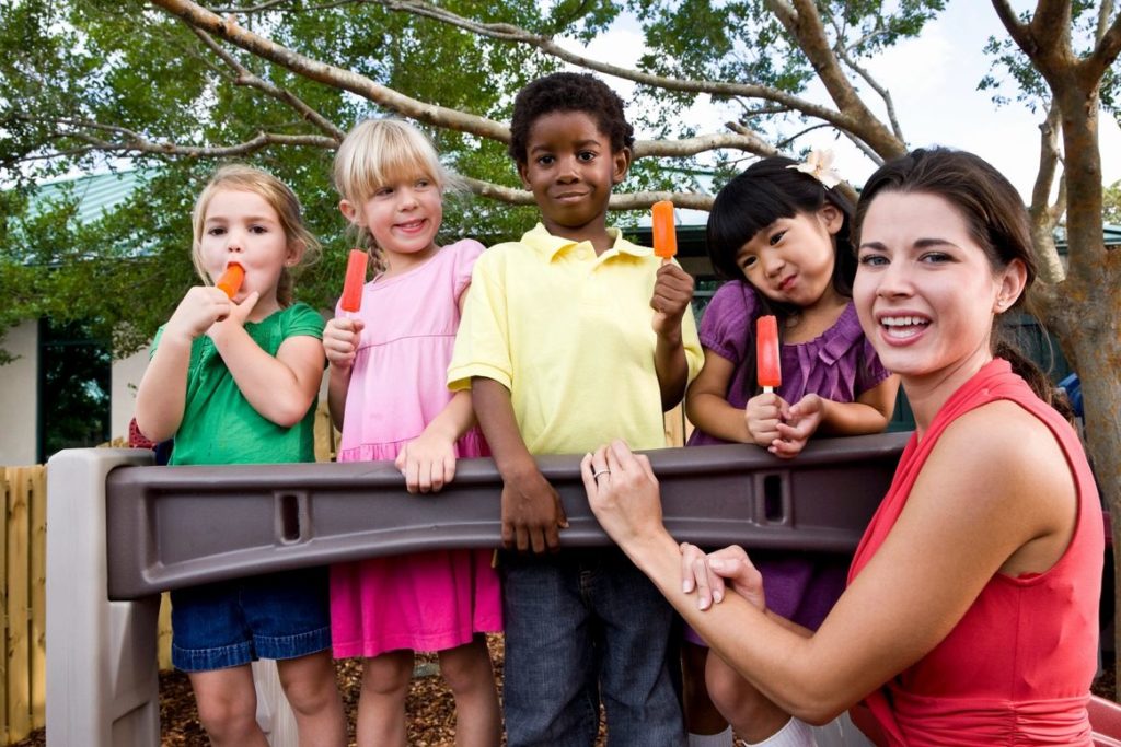 A group of children holding up popsicles in front of a woman.