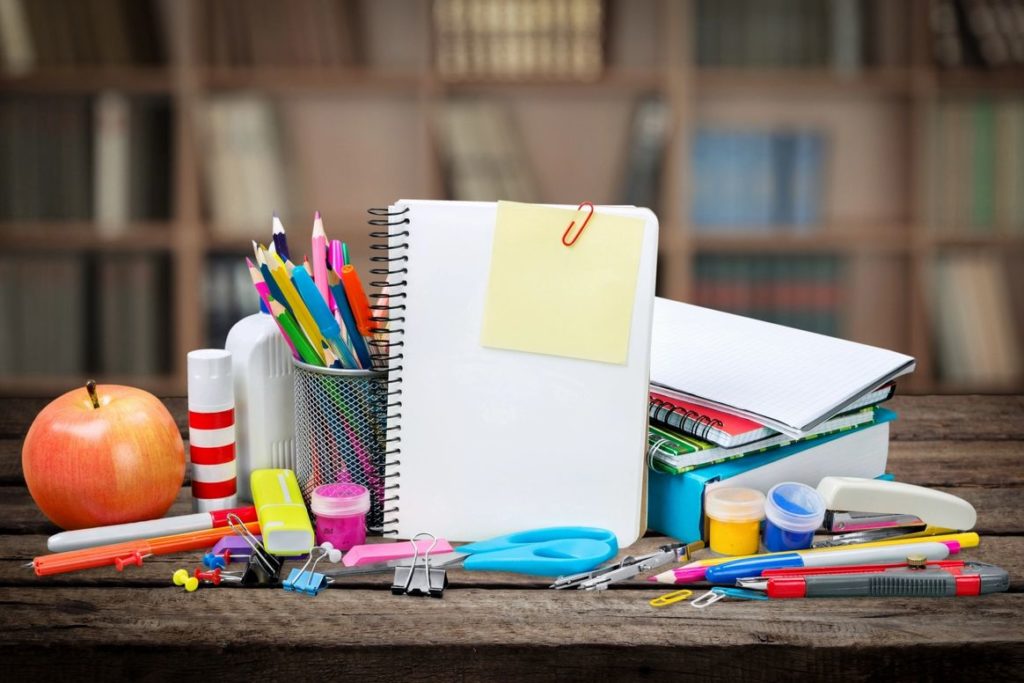 A desk with many school supplies and an open notebook.