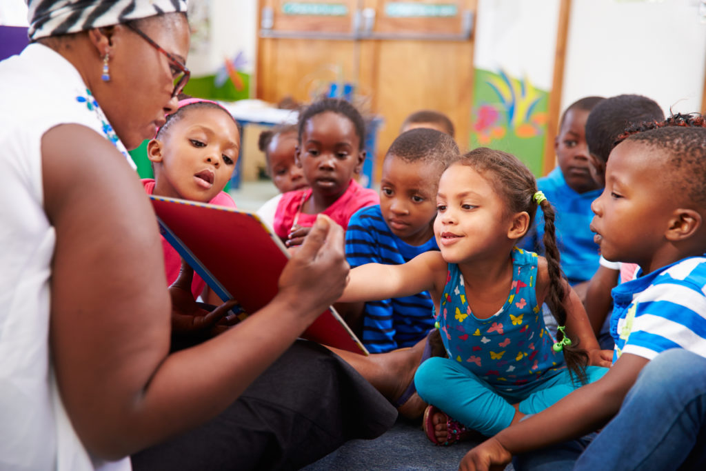 A group of children sitting around and one person reading.